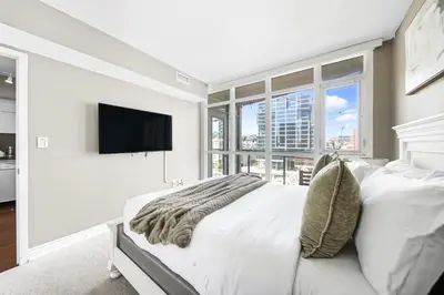 a white bedroom with a bed and a tv at Spacious Toronto Condo w Patio - City Comfort in Toronto