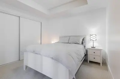 a white bedroom with a white bed and a night stand at Modern Down Town Condo Near CN Tower with Fast WiFi in Toronto