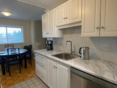a kitchen with white cabinets and a sink and a table at Bright 2 BR pet friendly, KING bed, WiFi,2 parking in Kitchener
