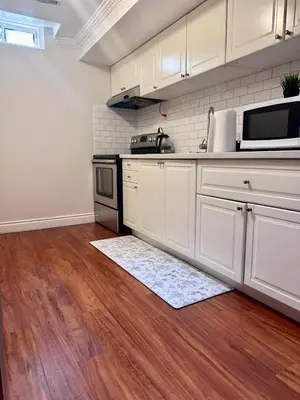 a kitchen with white cabinets and a wooden floor at Quincy Home in Mississauga