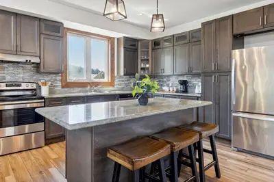 a kitchen with wooden cabinets and a large island with stools at 8 BR Luxury Swiss Style Chalet w Hot Tub in Blue Mountains