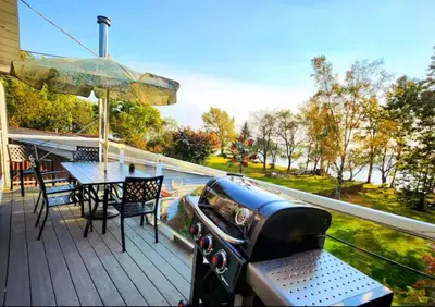 a deck with a table and chairs and an umbrella at Waterfront Comfy Guesthouse, PEC in Carrying Place