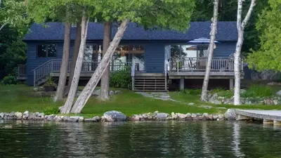 a blue house with a deck next to a body of water at Olga's Bay Lake House in Minett