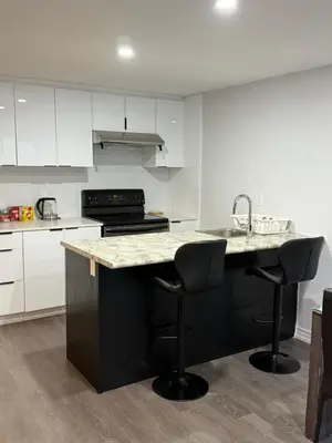 a kitchen with a black island with two bar stools at Comfy Basement Suite in Quiet Neighbourhood in Whitby