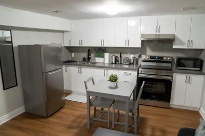 a kitchen with white cabinets and a table with chairs at Studio Apartment B - Full Kitchen - Cozy and Modern in Brampton