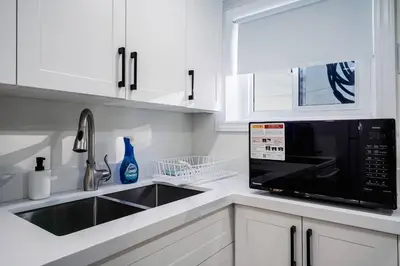 a white kitchen with a sink and a microwave at Bright & Cozy Home in the GTA (Basement Apartment) in Whitby