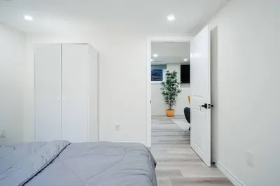 a white bedroom with a bed and a hallway at Bright & Cozy Home in the GTA (Basement Apartment) in Whitby