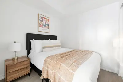 a white bedroom with a bed and a nightstand with a bed sidx sidx sidx at Bright 2BR Condo w Patio Central Toronto Retreat in Toronto