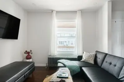 a living room with a black leather couch and a tv at Wood-Rich Niagara Loft close to Queen Street in Niagara Falls