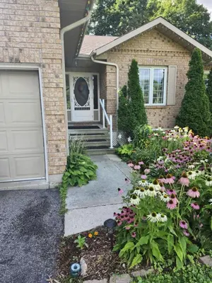 a house with a garage and flowers in front of it at White Rolling Sands of Penetang by Theatre in Penetanguishene