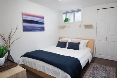 a white bedroom with a large bed with blue sheets at East Toronto BNB in Toronto