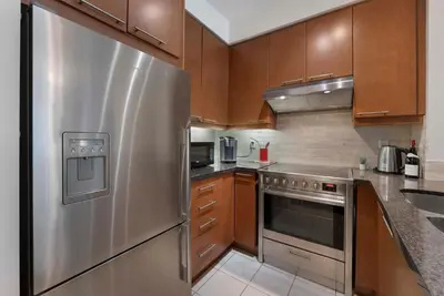 a kitchen with a stainless steel refrigerator and wooden cabinets at Luxury 1-Bedroom Condo in Yorkville, Downtown Toronto in Toronto