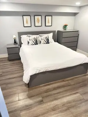 a bedroom with a bed with white sheets and wood floors at Soft Landing Spot Basement Hideout 2 bedroom apartment in Ajax