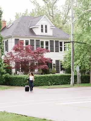 a woman walking in front of a white house at Guestroom in Old Town | Steps to Lake & Everything in Niagara on the Lake