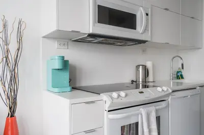 a white kitchen with a microwave above a stove at Stylish Modern Condo in the Heart of Toronto in Toronto