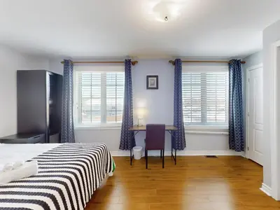 a bedroom with a bed and a desk and two windows at Cozy Queen room with Shared Bath near Seneca Finch 404 in Toronto