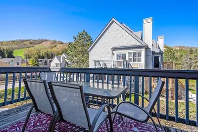 a table and chairs on a balcony with a house at Stay A While Ski-In-Out Hot Tub & Shuttle in Blue Mountains