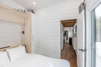 a bedroom with white walls and a bed and a window at The Hideaway - Tiny House in Flesherton