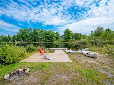 a wooden dock with a bench and a boat on a lake at Lakefront Muskoka Cottage with Fire Pit and BBQ in Port Carling