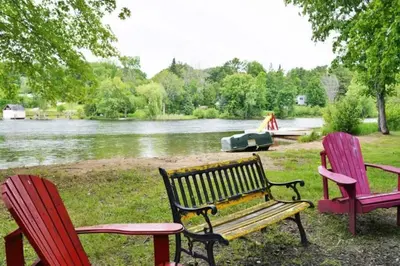 three chairs and a bench in front of a lake at Modern 4BR Lake Escape with Patio & BBQ Area in Kawartha Lakes