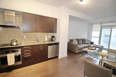 a kitchen with wooden cabinets and a living room at The Grand Avenue Suites - Downtown Toronto Entertainment District in Toronto
