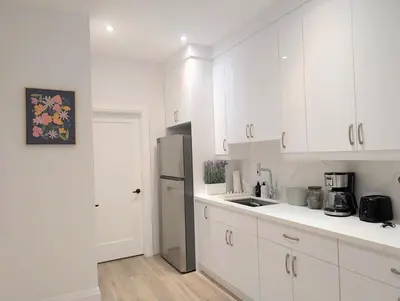 a white kitchen with white cabinets and a refrigerator at Luxury 1BR plus den walkout basement in Toronto