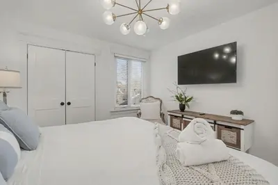 a white bedroom with a large bed and a television at Upscale Modern Home with Spa Pool in Niagara on the Lake