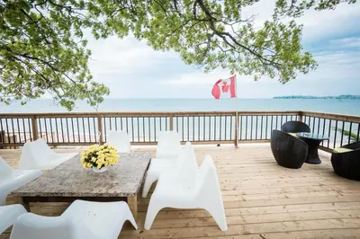 a table and white chairs on a deck with the ocean at Beach Front Family Cottage Ping Pong & Karaoke in Fort Erie