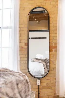 a mirror hanging on a brick wall with a bed at Bradshaw Lofts The Brixton King Suite in Stratford