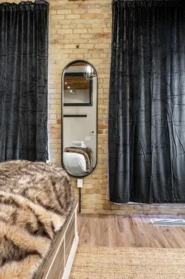 a room with a mirror and a bed in front of a brick wall at Bradshaw Lofts The Brixton King Suite in Stratford