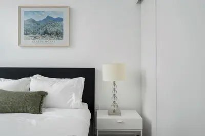 a bedroom with a white bed and a nightstand with a lamp at Modern 2 Bed Condo in the Junction+Parking in Toronto