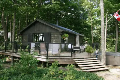 a cabin in the woods with a porch and stairs at Lake Eugenia Escape - Cozy Lakefront with Hot Tub in Flesherton
