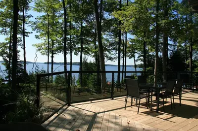 a deck with a table and chairs and a view of the water at Lake Eugenia Escape - Cozy Lakefront with Hot Tub in Flesherton