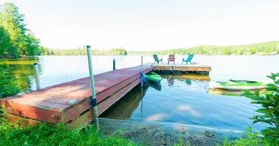 a dock with two chairs and a boat on a lake at Amazing Lakefront cottage on Paradise Lake in Haliburton