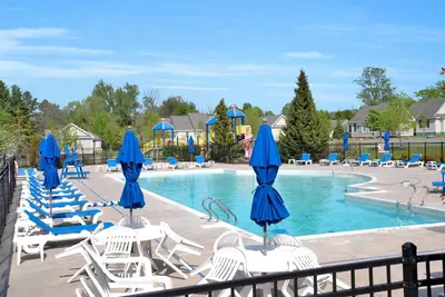 a swimming pool with chairs and blue umbrellas at The Juniper - 43 Butternut in Cherry Valley