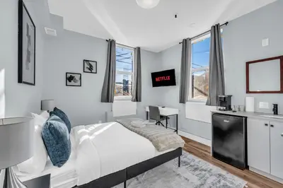 a white bedroom with a bed and a desk at Guestic at Queen West in Toronto