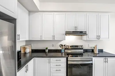 a white kitchen with black counter tops and white cabinets at Spacious 3BR House with Modern Comforts in Thorold