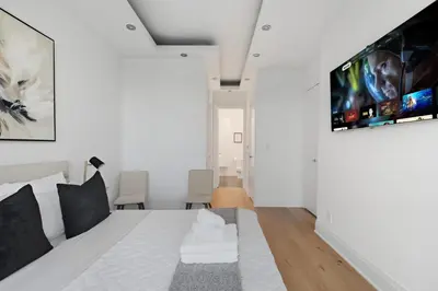 a white bedroom with a bed and a flat screen tv at Luxury Parklawn Penthouse Breathtaking Lake View in Toronto