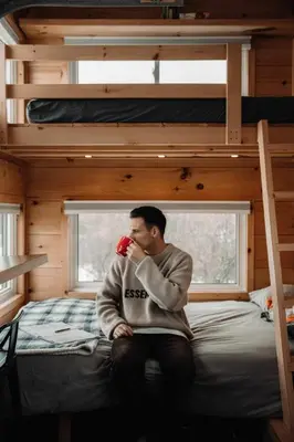 a man sitting on a bed in a tiny house at Woodrush Cabin a Charming Lakefront Tiny Cabin in Victoria Road