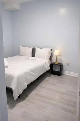 a bedroom with a bed with white sheets and a lamp at Modern 2BR Basement Suite Private Entrance in Brampton