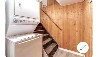 a small kitchen with a washer and dryer next to a wooden wall at Bright Room in Walkout Basement in Pickering