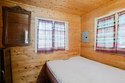 a small bedroom with a bed in a wooden cabin at Charming Lakeview Family Resort in Katchwanooka with Private BBQ and firepit in Lakefield