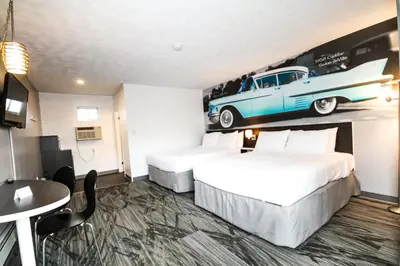 two beds in a hotel room with a car on the wall at Cadillac Motel Niagara in Niagara Falls