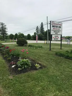 a sign for a motor inn with flowers in a field at Shenstone Motor Inn in Wiarton
