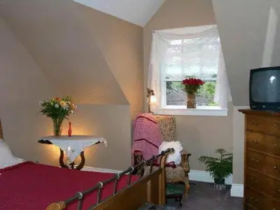 a bedroom with a bed and a tv and a chair at Antique Slumber Old Town Bed & Breakfast in Niagara on the Lake