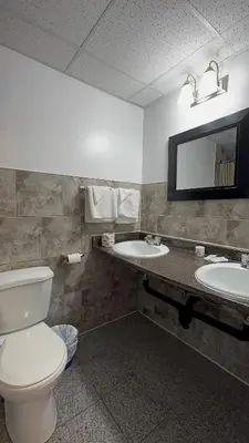 a bathroom with a toilet and two sinks and a mirror at Empress Inn and Suites by the Falls in Niagara Falls