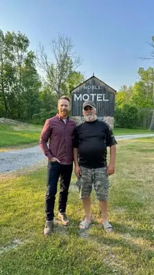 two men standing in the grass in front of a sign at Noble Motel in Norland