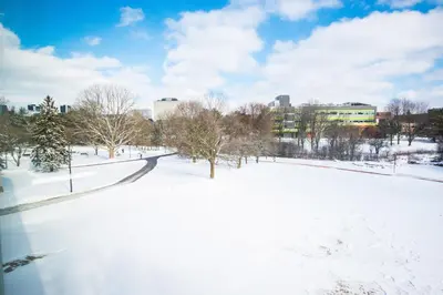 a park covered in snow with buildings in the background at United College in Waterloo