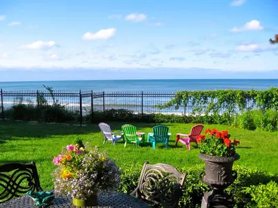 a yard with chairs and a table with the ocean in the background at Willowmere in Cobourg