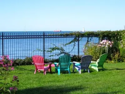 four colorful chairs sitting in the grass near a fence at Willowmere in Cobourg
